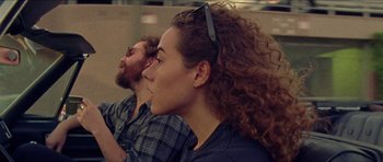 Movie still from “Bliss” (2019), directed by Joe Begos – A man and a woman sitting next to each other; Close Up shot, Over the shoulder angle