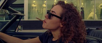 Movie still from “Bliss” (2019), directed by Joe Begos – A woman sitting in a car smoking a cigarette; Close Up shot, Over the shoulder angle