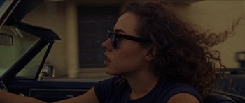 Movie still from “Bliss” (2019), directed by Joe Begos – A woman wearing sunglasses looking off into the distance; Close Up shot, Over the shoulder angle