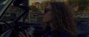 Movie still from “Bliss” (2019), directed by Joe Begos – A woman with curly hair is holding a cell phone; Close Up shot, Low angle