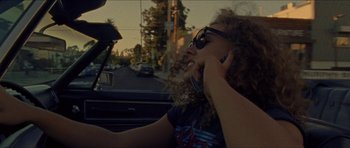 Movie still from “Bliss” (2019), directed by Joe Begos – A woman in sunglasses talking on a cell phone while sitting in a car; Close Up shot, High angle