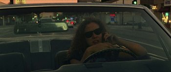 Movie still from “Bliss” (2019), directed by Joe Begos – A woman sitting in the back seat of a car talking on a cell phone; Medium shot, High angle