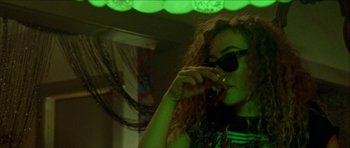 Movie still from “Bliss” (2019), directed by Joe Begos – A woman with curly red hair wearing sunglasses and holding a cigarette; Medium shot, Over the shoulder angle