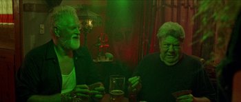 Movie still from “Bliss” (2019), directed by Joe Begos – Two men sitting at a table in front of a glass of beer; Medium shot, Low angle