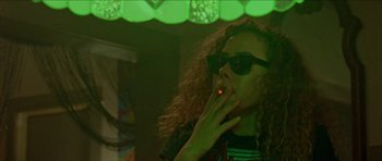 Movie still from “Bliss” (2019), directed by Joe Begos – A woman with curly hair and sunglasses smoking a cigarette; Medium shot, Low angle