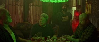 Movie still from “Bliss” (2019), directed by Joe Begos – A man sitting at a table in front of a green light; Medium shot, Over the shoulder angle