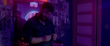 Movie still from “Bliss” (2019), directed by Joe Begos – A man standing next to a wall covered in pictures; Medium shot, Low angle