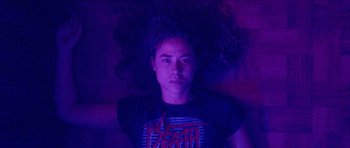 Movie still from “Bliss” (2019), directed by Joe Begos – A man with long curly hair is laying in a purple room; Medium shot, Low angle