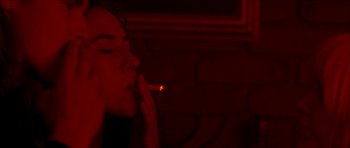 Movie still from “Bliss” (2019), directed by Joe Begos – A woman is smoking a cigarette in a dark room; Close Up shot, Over the shoulder angle