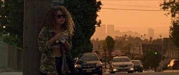Movie still from “Bliss” (2019), directed by Joe Begos – A woman standing on the side of a road holding a cell phone; Wide shot, Over the shoulder angle