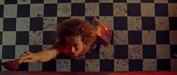 Movie still from “Bliss” (2019), directed by Joe Begos – A woman is laying on the floor holding a box; Wide shot, Overhead angle