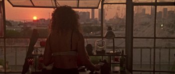 Movie still from “Bliss” (2019), directed by Joe Begos – A woman standing in front of a window with a city view; Wide shot, High angle