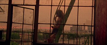 Movie still from “Bliss” (2019), directed by Joe Begos – A woman sitting on top of a swing in front of a window; Wide shot, Low angle