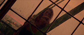 Movie still from “Bliss” (2019), directed by Joe Begos – A woman with long curly hair standing in front of a window; Medium shot, Low angle