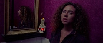 Movie still from “Bliss” (2019), directed by Joe Begos – A woman standing in front of a mirror with a candle in the shape of a human skull; Close Up shot, Low angle
