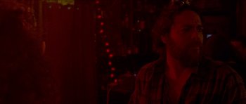 Movie still from “Bliss” (2019), directed by Joe Begos – A man sitting at a table in front of lights; Close Up shot, Over the shoulder angle