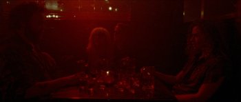 Movie still from “Bliss” (2019), directed by Joe Begos – A man and a woman sitting in front of a table; Wide shot, Overhead angle