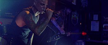 Movie still from “Bliss” (2019), directed by Joe Begos – A man with a microphone and a man playing a guitar; Medium shot, Low angle