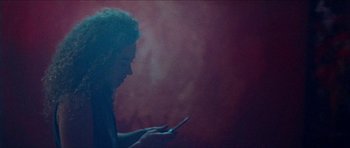 Movie still from “Bliss” (2019), directed by Joe Begos – A woman is looking at her cell phone in the dark; Medium shot, Low angle