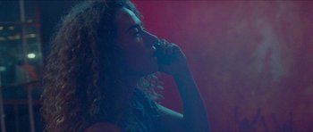 Movie still from “Bliss” (2019), directed by Joe Begos – A woman with long curly hair is holding a microphone up to her mouth; Close Up shot, Low angle