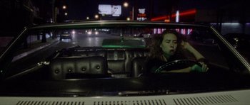 Movie still from “Bliss” (2019), directed by Joe Begos – A woman sitting in the back seat of a car at night; Wide shot, High angle