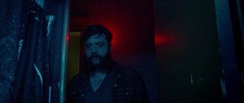 Movie still from “Bliss” (2019), directed by Joe Begos – A man with a long beard standing in a dark room; Close Up shot, Low angle