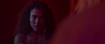 Movie still from “Bliss” (2019), directed by Joe Begos – A woman with curly hair is looking at the camera; Close Up shot, Over the shoulder angle