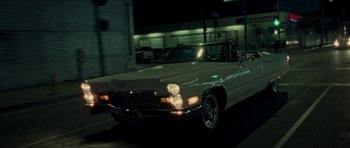 Movie still from “Bliss” (2019), directed by Joe Begos – An old car is driving down the street at night; Wide shot, High angle