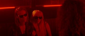 Movie still from “Bliss” (2019), directed by Joe Begos – Two women are posing for a picture in a dark room; Medium shot, Over the shoulder angle