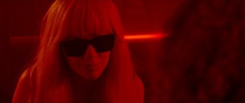 Movie still from “Bliss” (2019), directed by Joe Begos – A woman wearing sunglasses in a red room; Close Up shot, Low angle