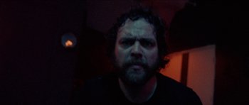 Movie still from “Bliss” (2019), directed by Joe Begos – A man with a scruffy beard stares at the camera; Close Up shot, Low angle