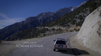 Movie still from “Blue Jay” (2016), directed by Alex Lehmann – A car driving down a road in front of a mountain range; Extreme Wide shot, Low angle