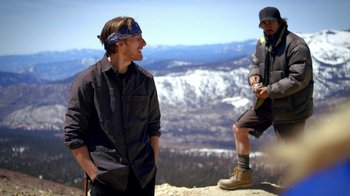 Movie still from “Blue Jay” (2016), directed by Alex Lehmann – A man standing on top of a mountain next to another man; Wide shot, Low angle