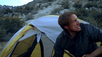 Movie still from “Blue Jay” (2016), directed by Alex Lehmann – A man in a black shirt is outside a tent; Medium shot, Over the shoulder angle
