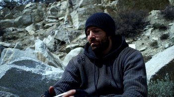Movie still from “Blue Jay” (2016), directed by Alex Lehmann – A man sitting on the ground in front of some rocks; Medium shot, High angle