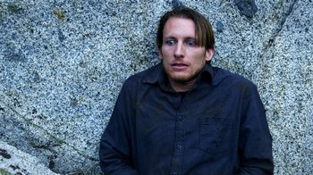 Movie still from “Blue Jay” (2016), directed by Alex Lehmann – A man in a black shirt is sitting against a stone wall; Close Up shot, High angle