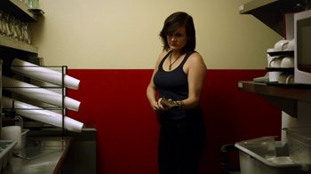 Movie still from “Blue Jay” (2016), directed by Alex Lehmann – A woman standing in front of a red wall holding papers; Medium shot, Low angle