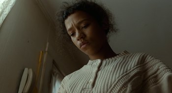 Movie still from “Bones and All” (2022), directed by Luca Guadagnino – A young woman in a white sweater looking down; Close Up shot, Low angle