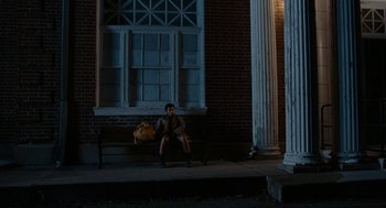 Movie still from “Bones and All” (2022), directed by Luca Guadagnino – A person sitting on a bench in front of a building; Extreme Wide shot, Low angle
