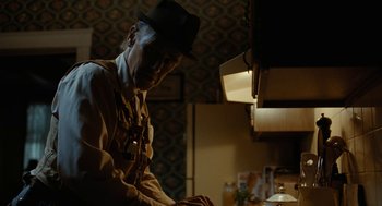 Movie still from “Bones and All” (2022), directed by Luca Guadagnino – An old man wearing a black hat in a kitchen; Medium shot, Over the shoulder angle