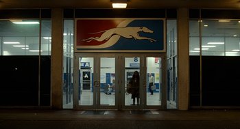 Movie still from “Bones and All” (2022), directed by Luca Guadagnino – A woman is standing in front of a store entrance; Wide shot, Low angle