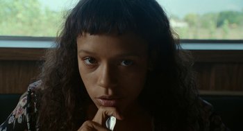 Movie still from “Bones and All” (2022), directed by Luca Guadagnino – A young woman with long black curly hair is holding her finger to her lips; Close Up shot, Low angle