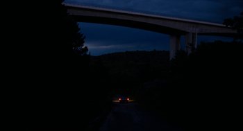 Movie still from “Bones and All” (2022), directed by Luca Guadagnino – A car driving down a road under a bridge; Extreme Wide shot, High angle
