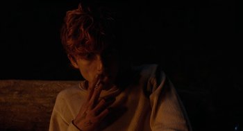Movie still from “Bones and All” (2022), directed by Luca Guadagnino – A person smoking a cigarette in a dark room; Close Up shot, Over the shoulder angle