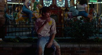 Movie still from “Bones and All” (2022), directed by Luca Guadagnino – A man sitting on the ground drinking a drink; Medium shot, Over the shoulder angle