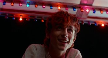 Movie still from “Bones and All” (2022), directed by Luca Guadagnino – A young man with red hair smiling for the camera; Close Up shot, Over the shoulder angle