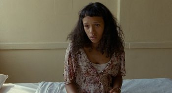 Movie still from “Bones and All” (2022), directed by Luca Guadagnino – A woman with long black curly hair sitting on a bed; Close Up shot, High angle