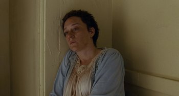 Movie still from “Bones and All” (2022), directed by Luca Guadagnino – A woman wearing a blue jacket is sitting in a corner; Close Up shot, High angle