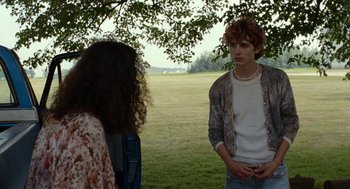 Movie still from “Bones and All” (2022), directed by Luca Guadagnino – A man and a woman standing under a tree in a field; Medium shot, Over the shoulder angle