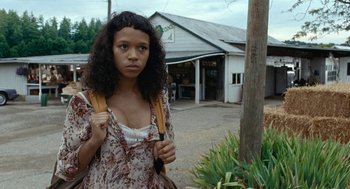 Movie still from “Bones and All” (2022), directed by Luca Guadagnino – A young woman with a backpack is standing in front of a building; Close Up shot, Low angle